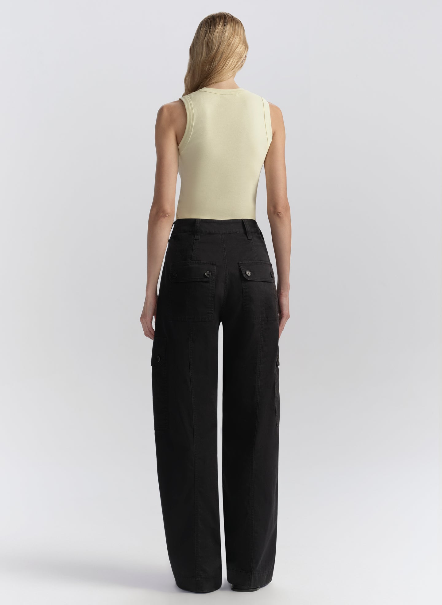 Woman wearing a light-colored sleeveless top and blue wide-leg pants on a white background