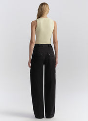 Woman wearing a light-colored sleeveless top and blue wide-leg pants on a white background