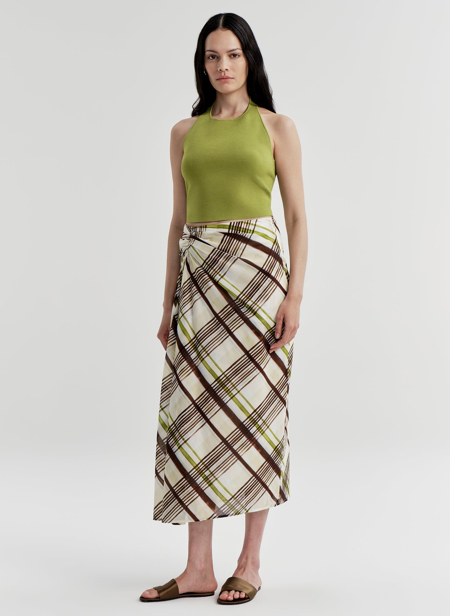 Woman wearing a green halter top and plaid skirt on a light gray background