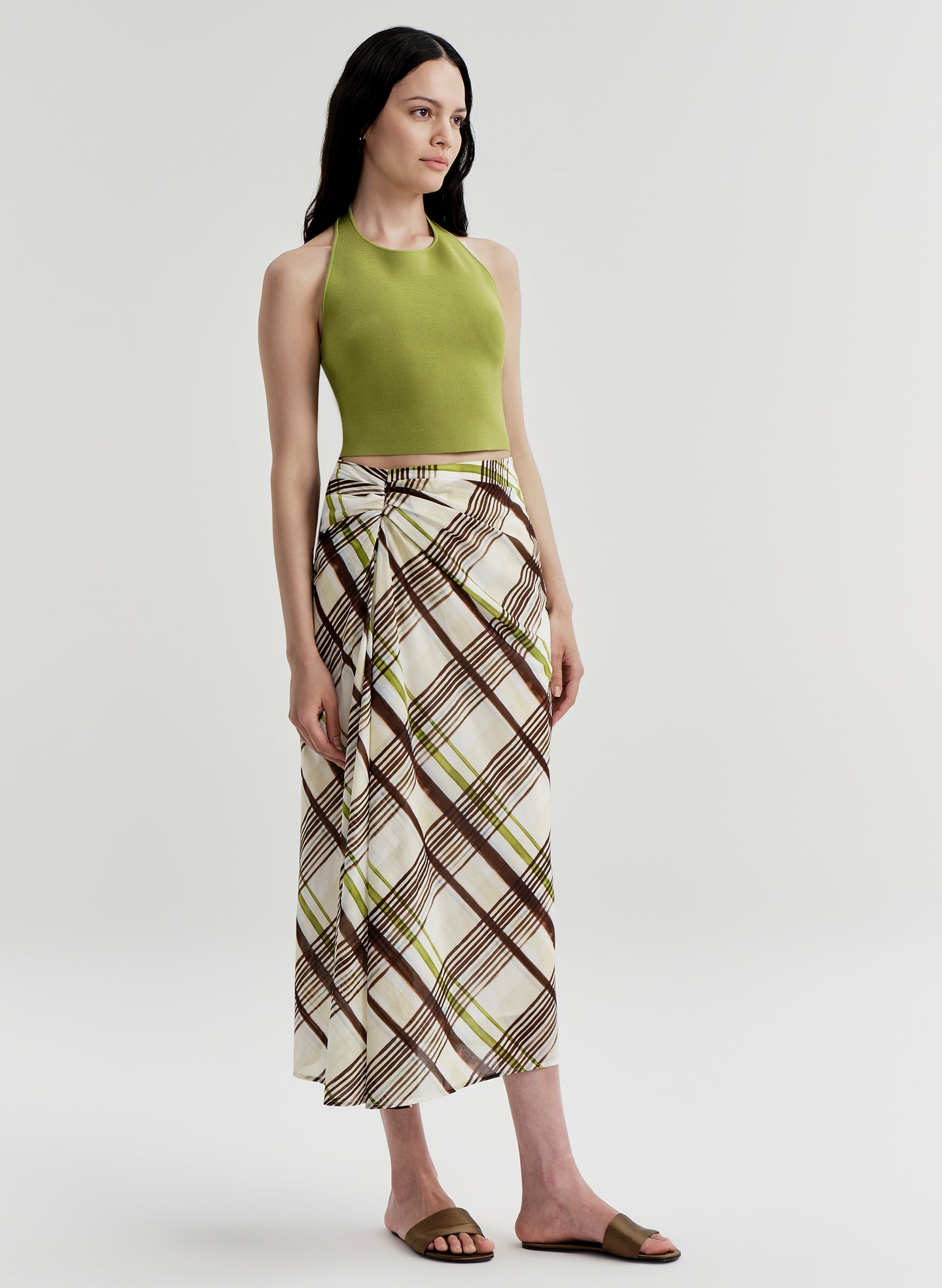 Woman wearing a green halter top and plaid skirt on a light gray background