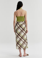 Woman wearing a green backless halter top and plaid skirt on a light gray background
