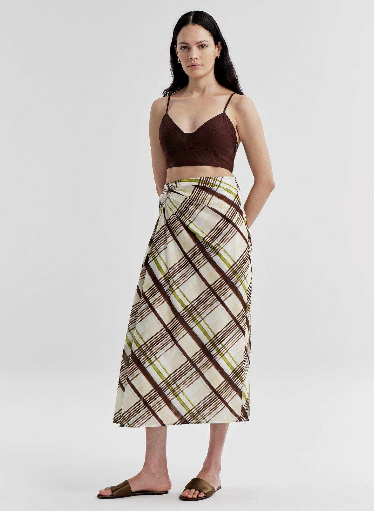 Woman wearing a brown and green plaid skirt with a plain background