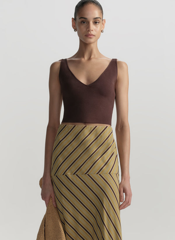 Woman wearing a brown top and a long, patterned skirt on a plain background