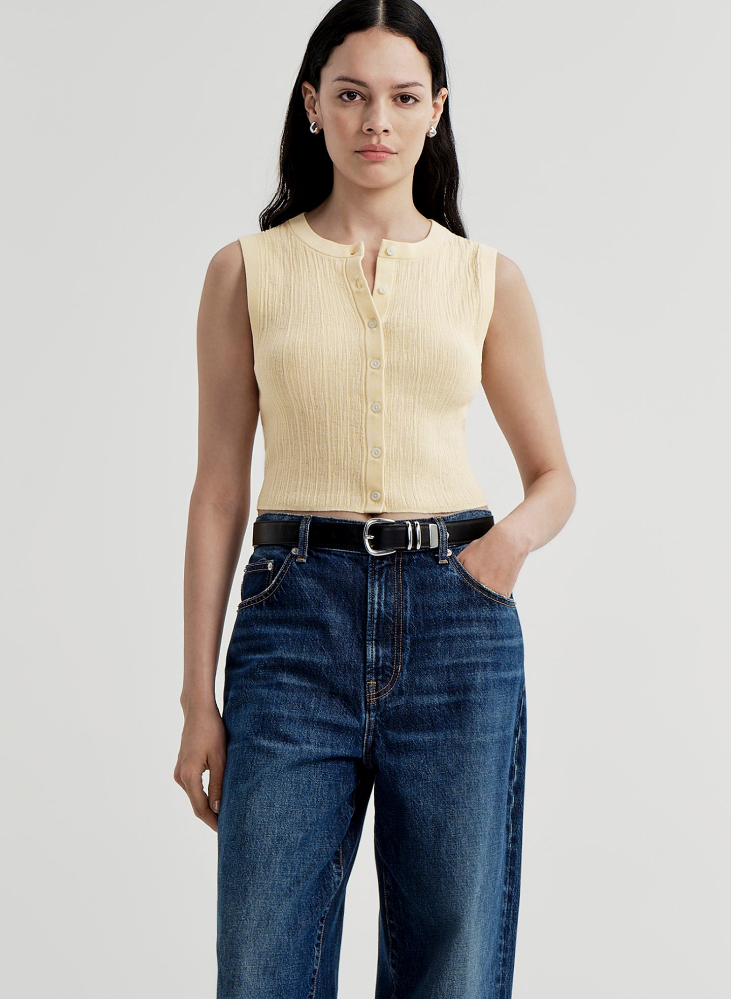Woman wearing a yellow sleeveless top and blue jeans on a plain background