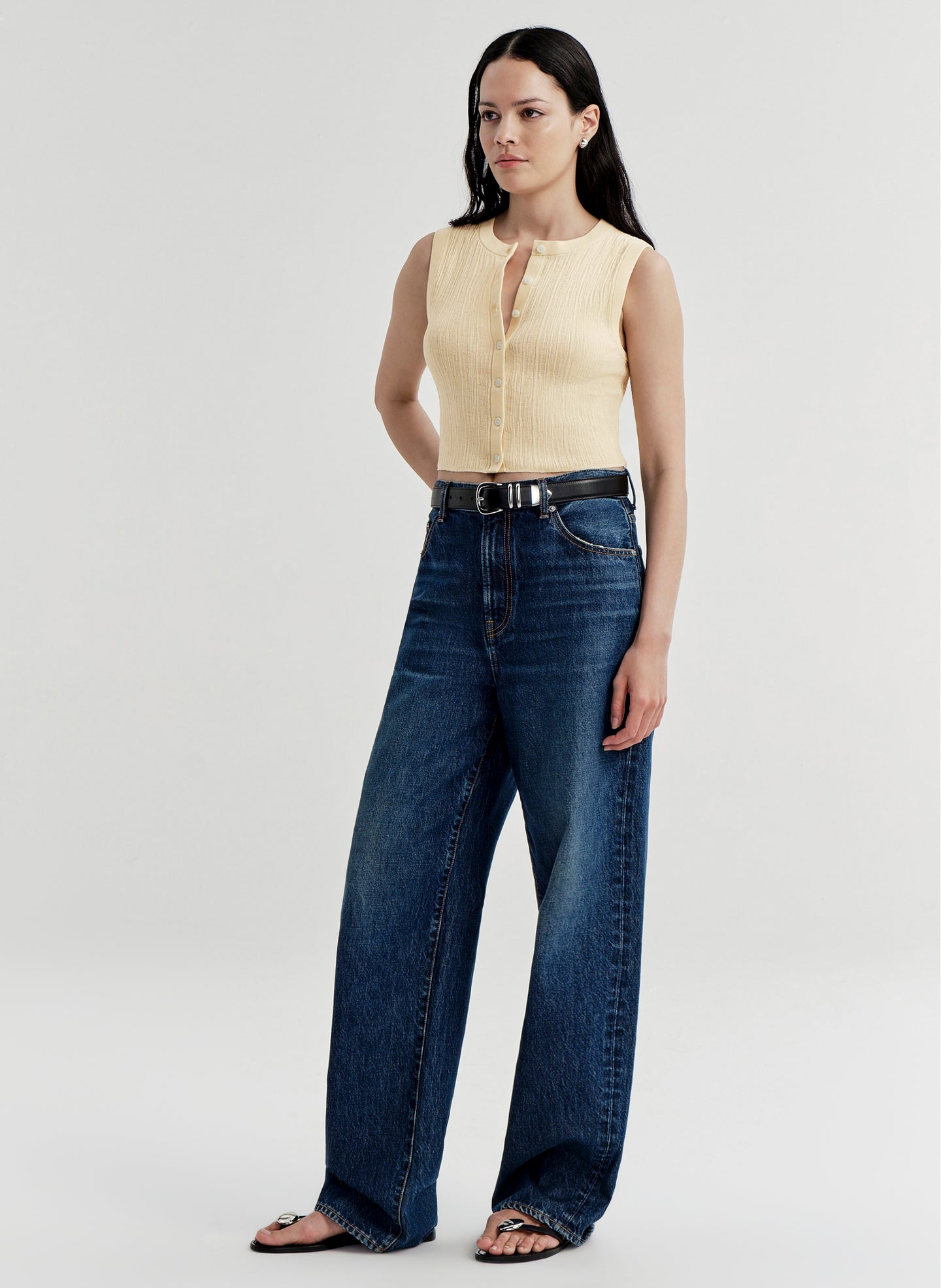 Woman wearing a yellow sleeveless top and blue jeans on a white background