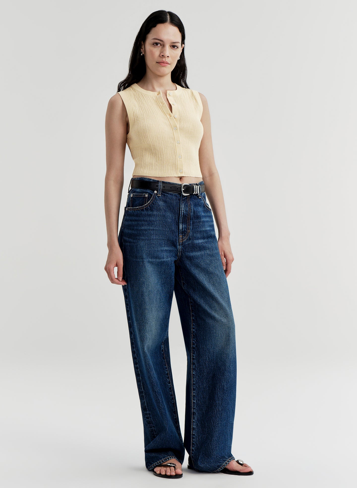 Woman wearing a yellow sleeveless top and blue jeans on a white background