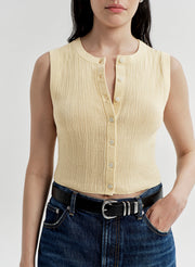 Woman wearing a yellow sleeveless top and blue jeans against a white background