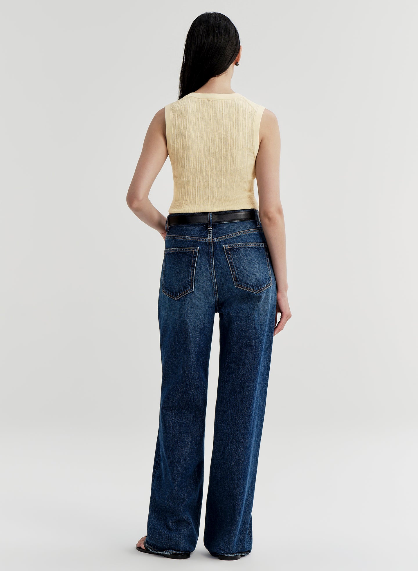 Person wearing blue jeans and a yellow top on a plain background