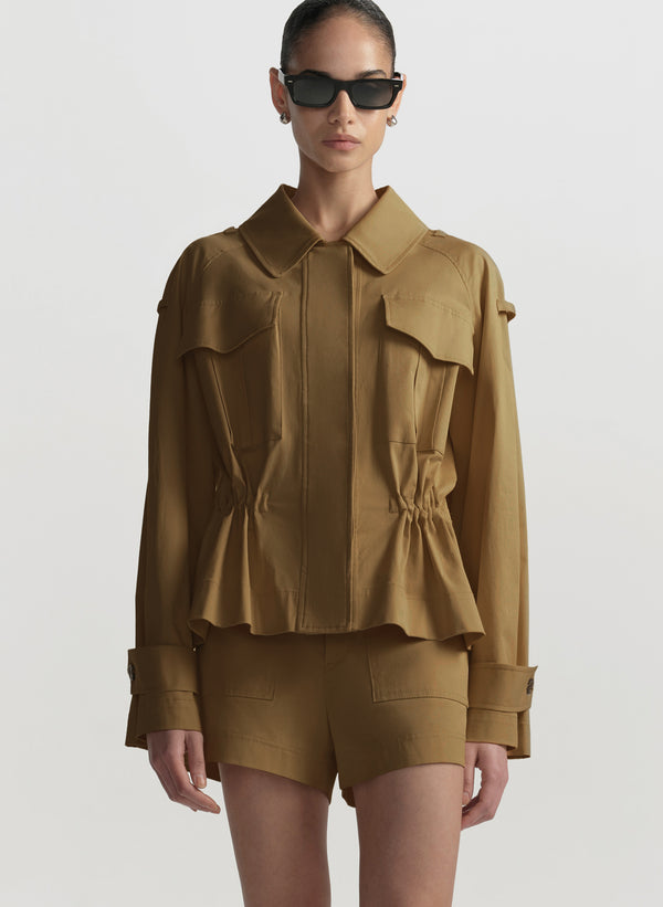 Person wearing a brown jacket and shorts set with sunglasses on a white background