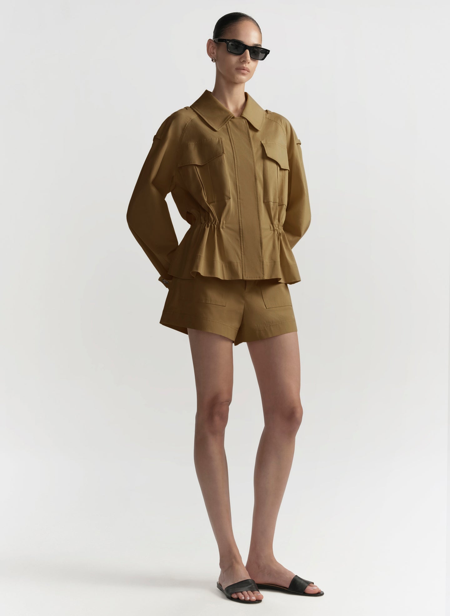 Woman wearing a hazel brown outfit with sunglasses on a white background