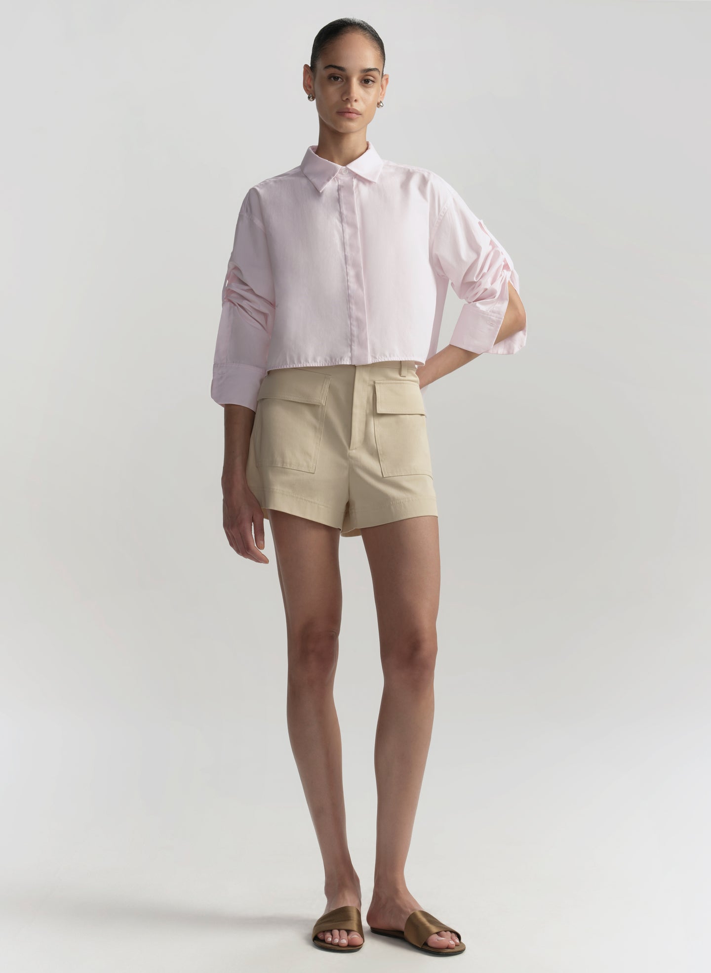 Woman wearing a light pink shirt and beige shorts on a white background