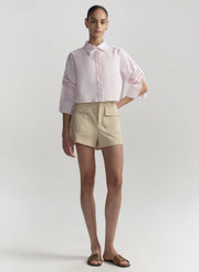 Woman wearing a light pink shirt and beige shorts on a white background