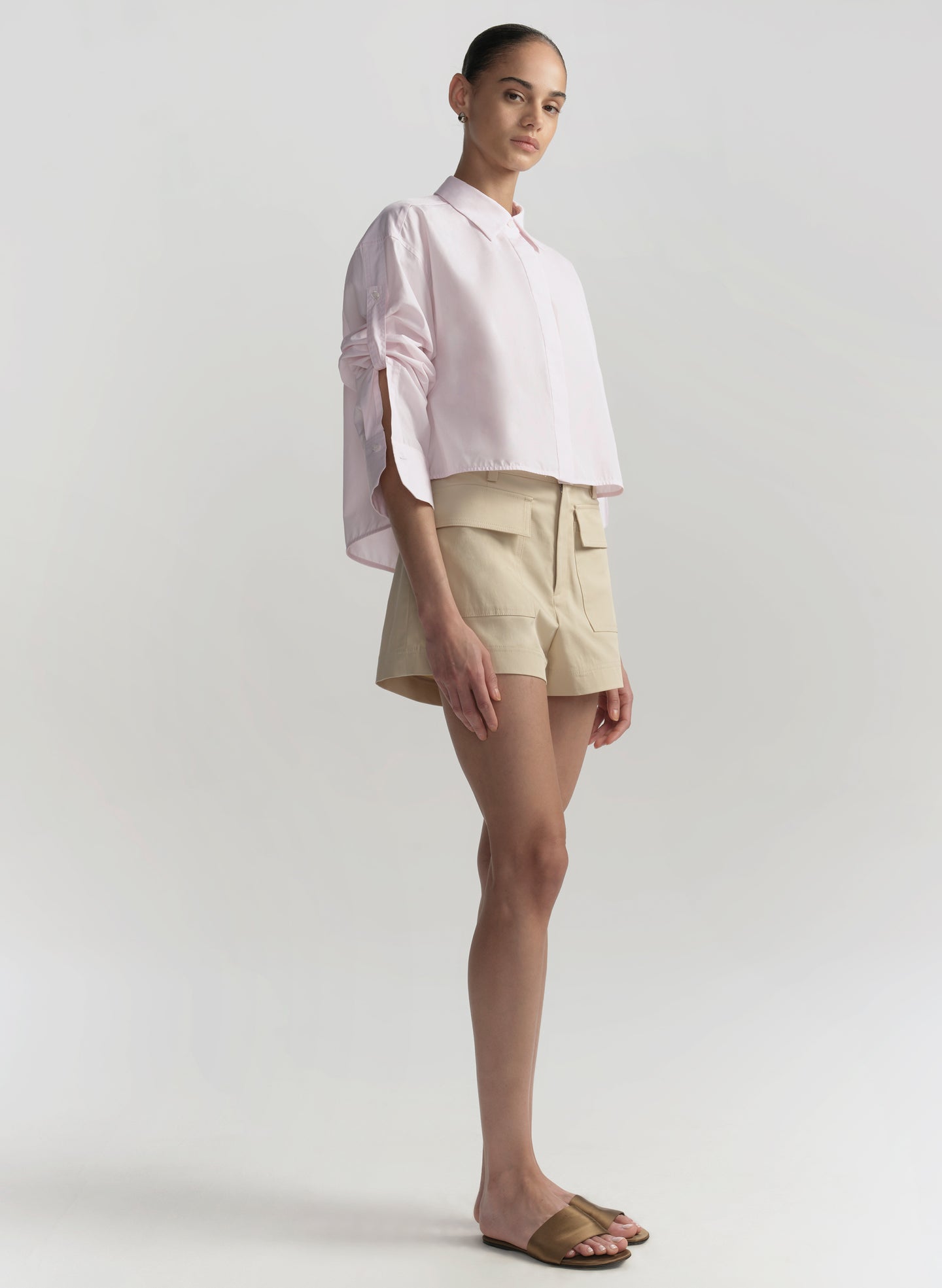 Woman wearing a light pink blouse and beige shorts on a white background