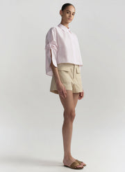 Woman wearing a light pink blouse and beige shorts on a white background
