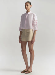 Woman wearing a light pink shirt and beige shorts on a plain background