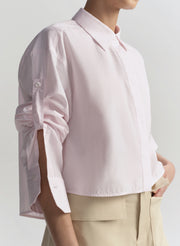 Person wearing a light pink blouse with rolled-up sleeves on a plain background