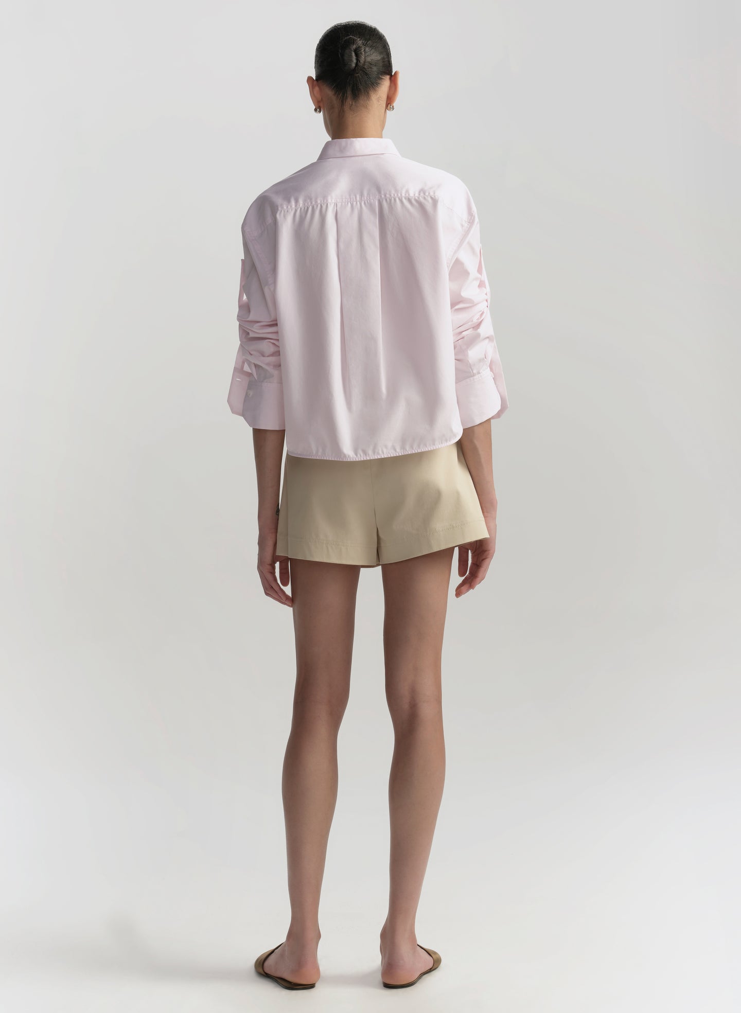 Person wearing a pink shirt and beige shorts on a plain background