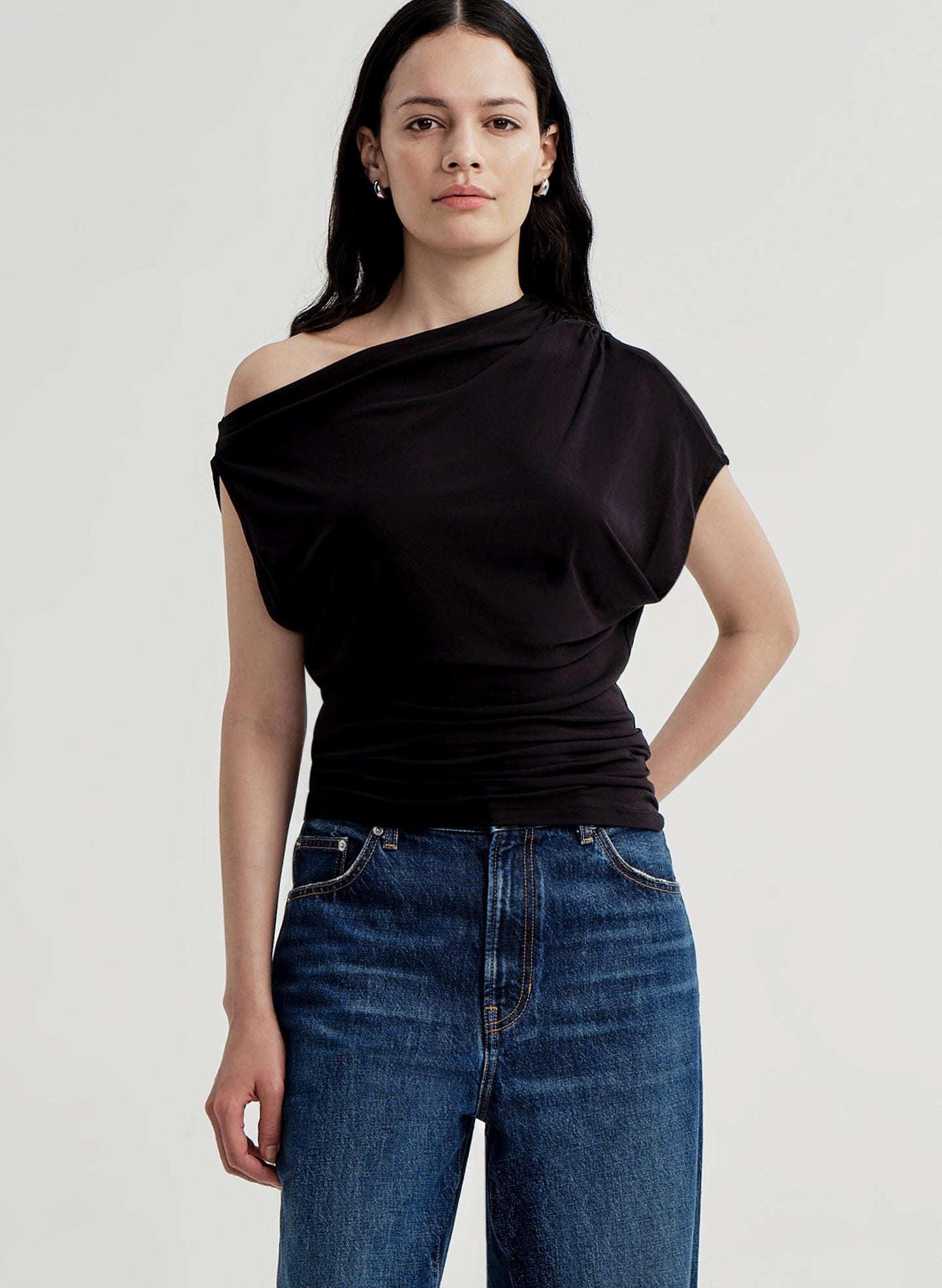 Woman wearing a black off-shoulder top and blue jeans on a light gray background