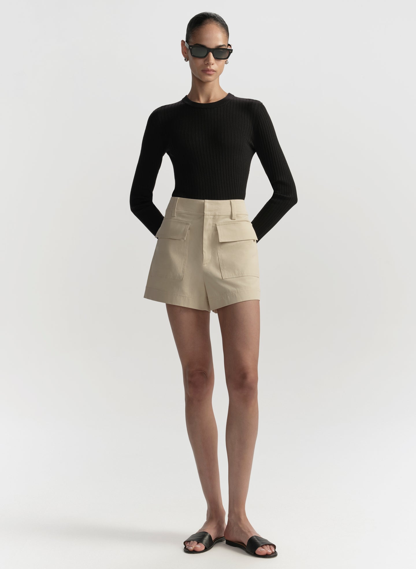 Woman wearing a black long-sleeve top and beige shorts on a white background