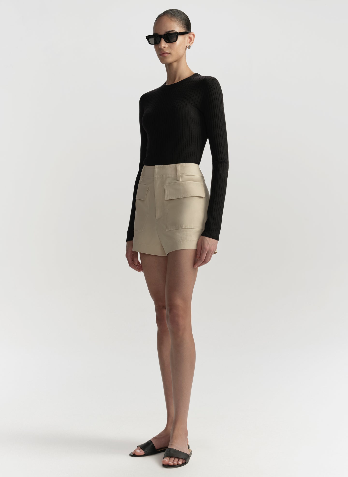 Person wearing a black long-sleeve top and beige shorts on a white background