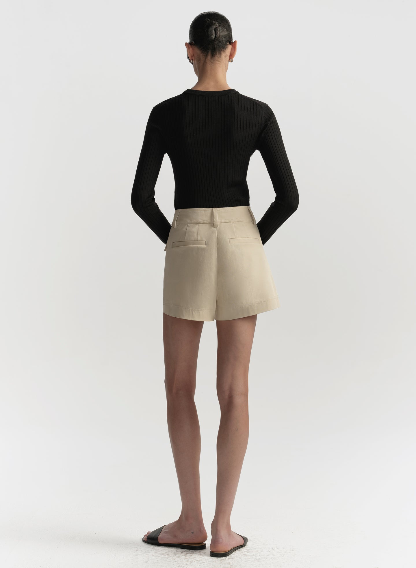 Person wearing a black long-sleeve top and beige shorts on a white background