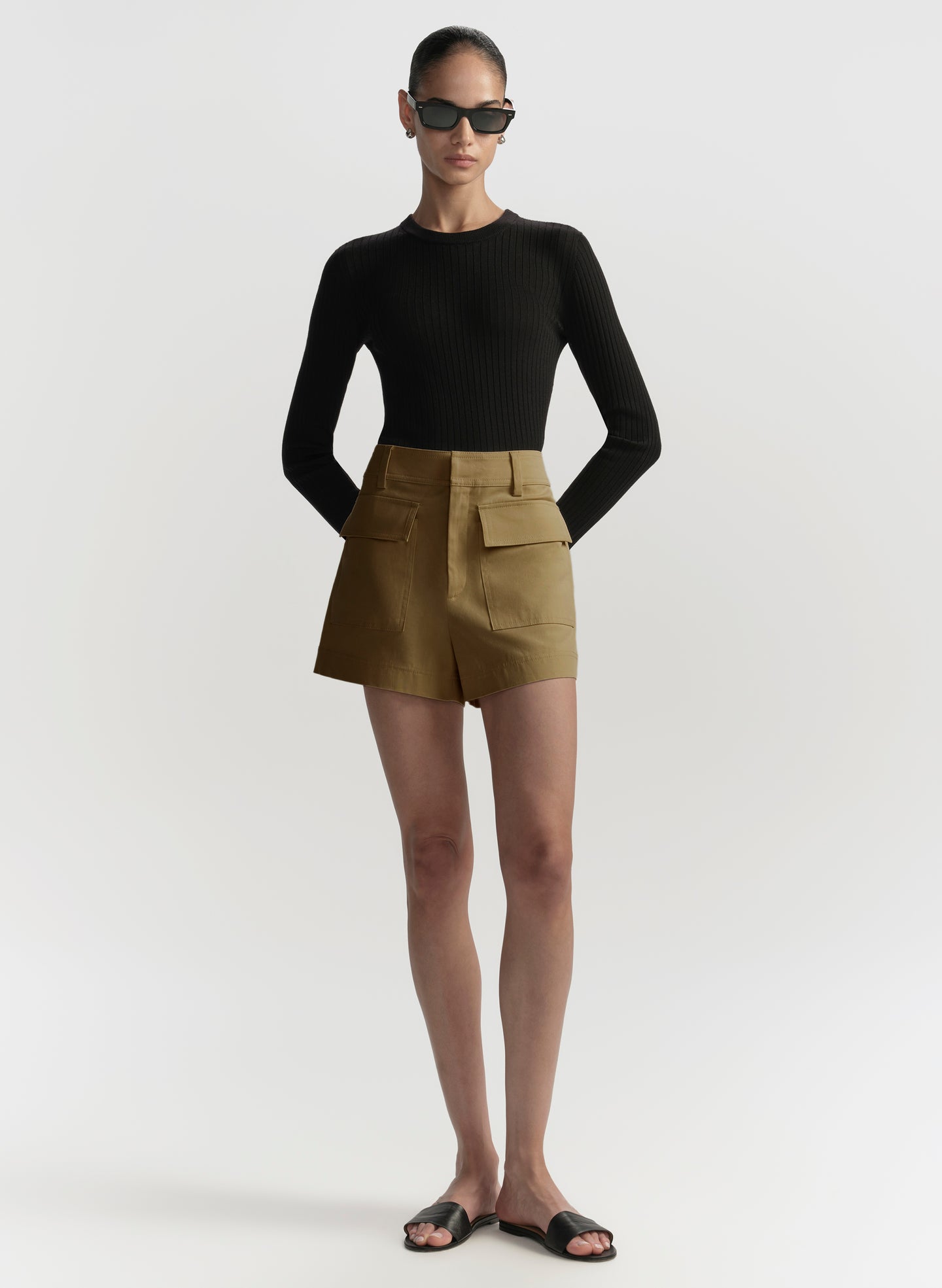 Person wearing a black top and beige shorts on a white background