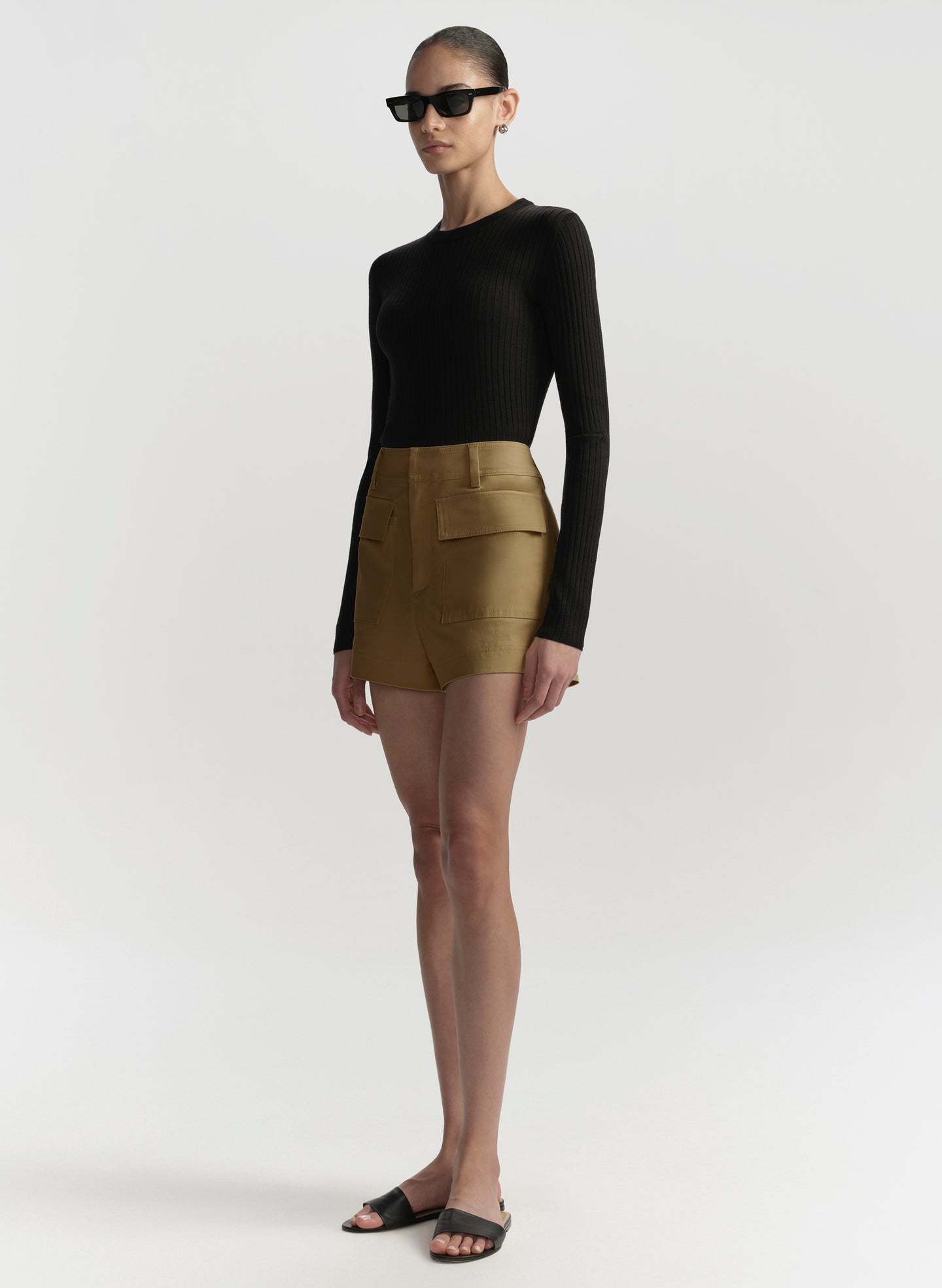 Person wearing a black long-sleeve top and hazel shorts on a white background