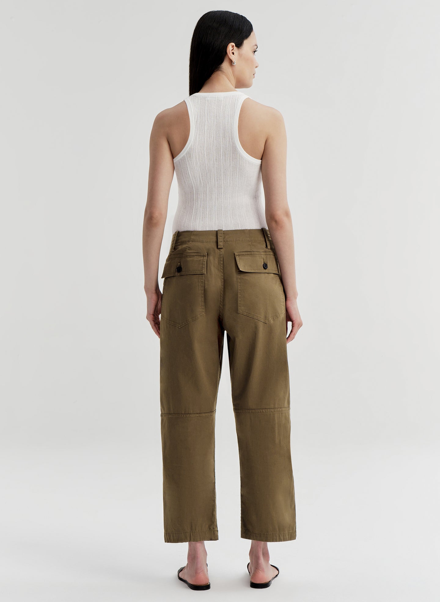 Woman wearing a white sleeveless top and olive green pants on a white background