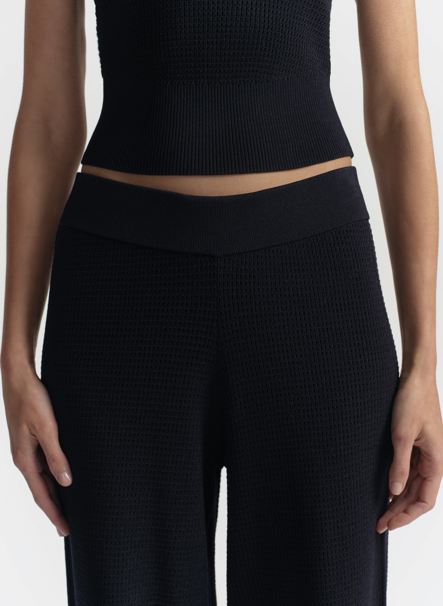 Person wearing a blue ribbed crop top and pants on a white background