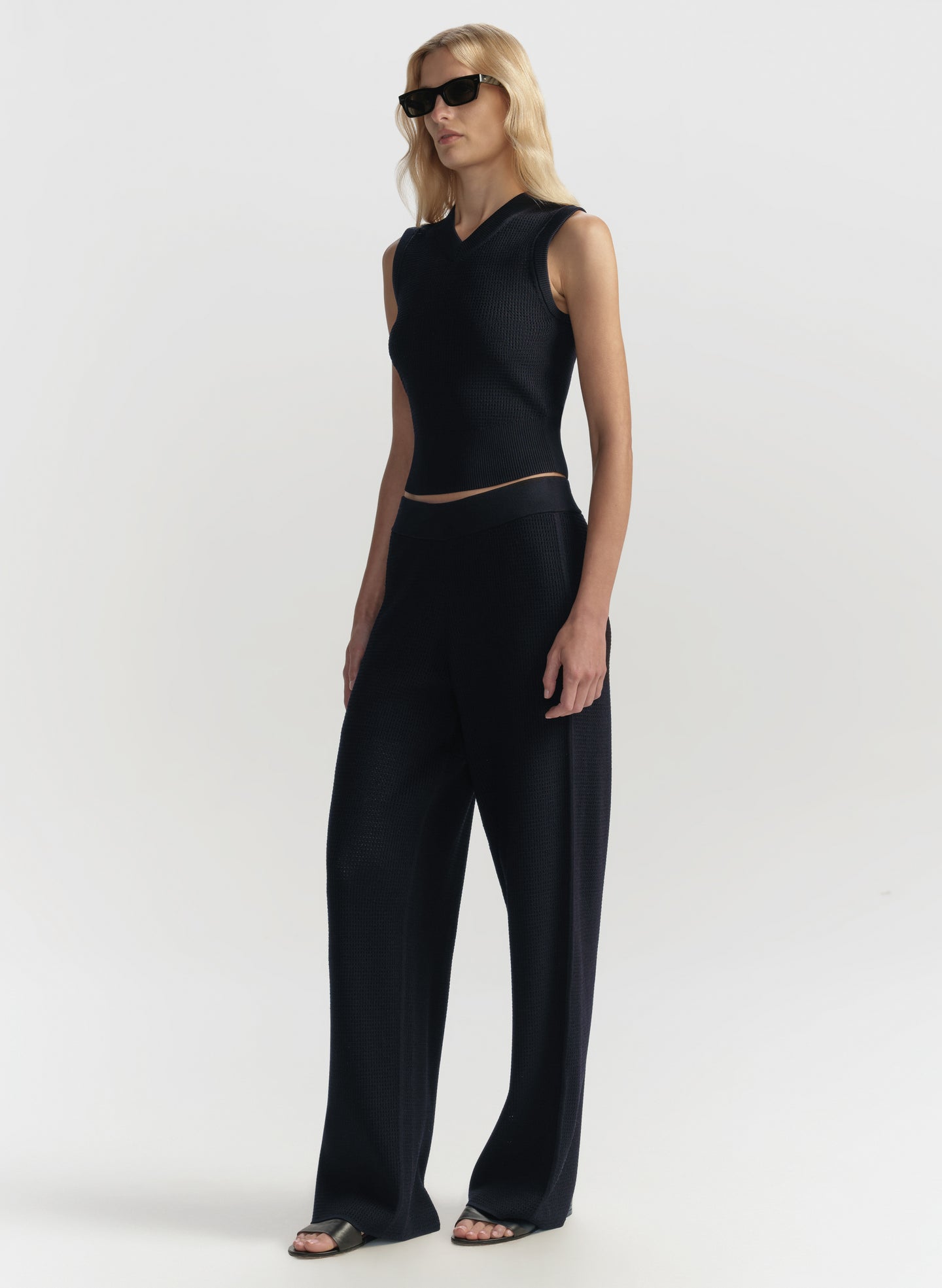 Person wearing a blue sleeveless top and wide-leg pants on a white background