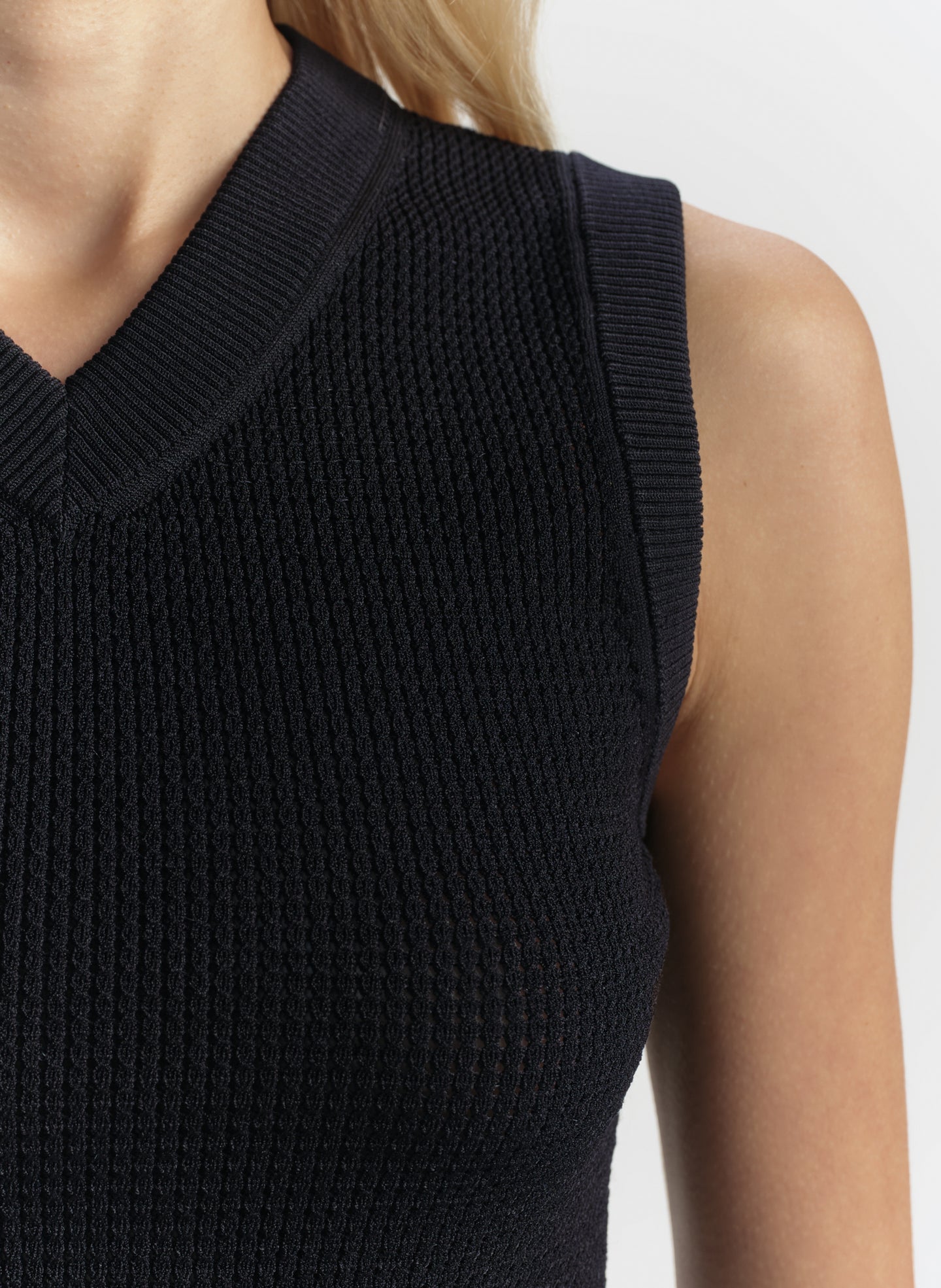 Blue sleeveless knitted top worn by a person on a white background