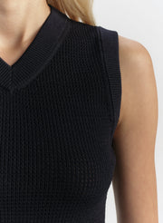 Blue sleeveless knitted top worn by a person on a white background