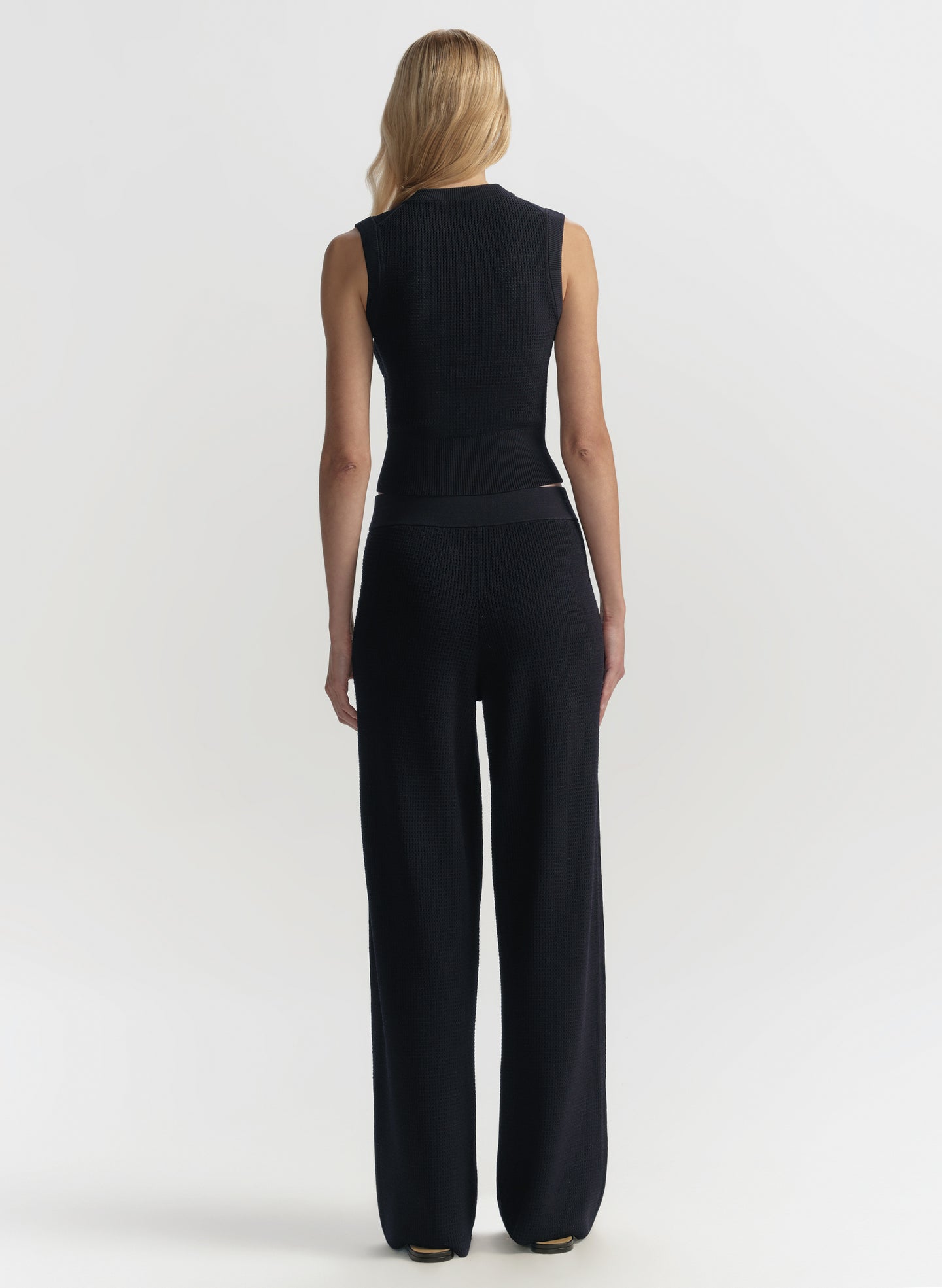 Woman wearing a blue sleeveless top and wide-leg pants on a white background