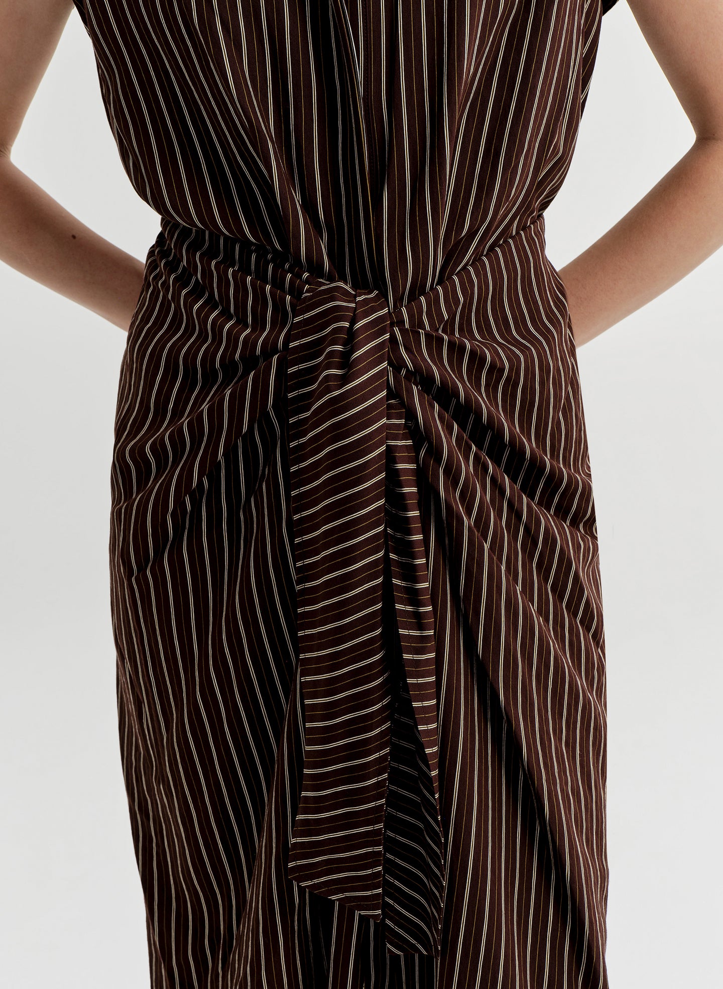 Brown and white striped dress with a tie waist on a plain background