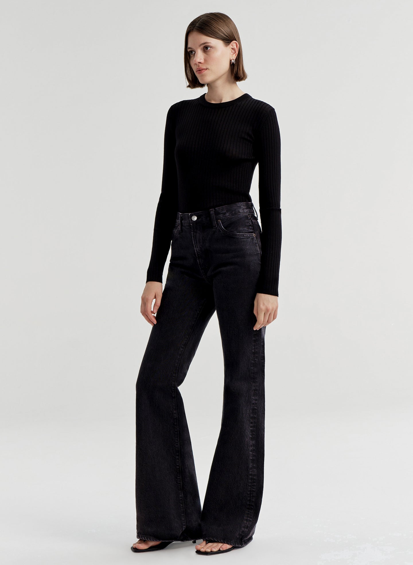 Woman wearing black flared jeans and a black top on a white background