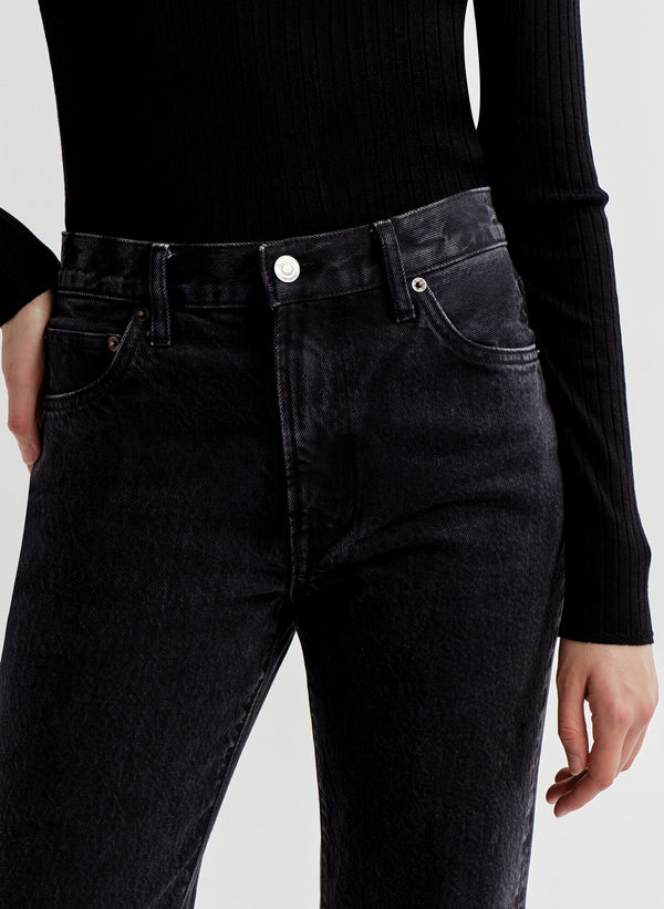 Person wearing black high-waisted jeans and a black long-sleeve top on a white background