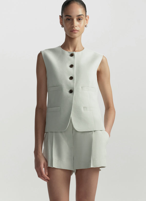 Woman wearing a light green sleeveless blazer and shorts on a white background