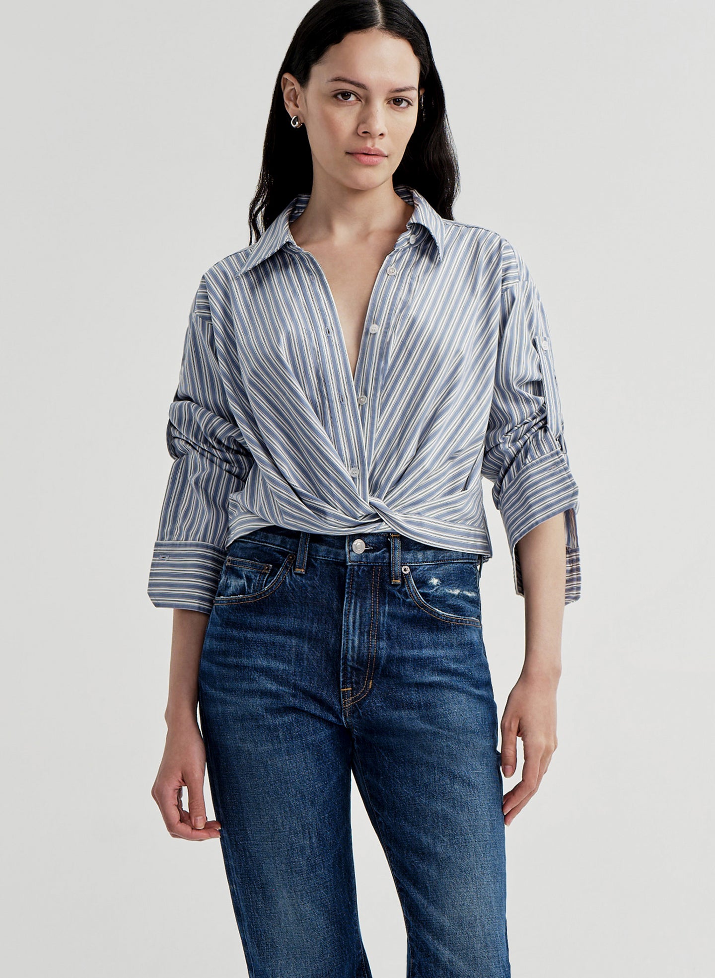 Woman wearing a striped shirt and blue jeans on a light gray background