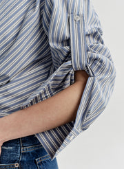 Close-up of a person wearing a blue and white striped shirt with rolled-up sleeves on a plain background