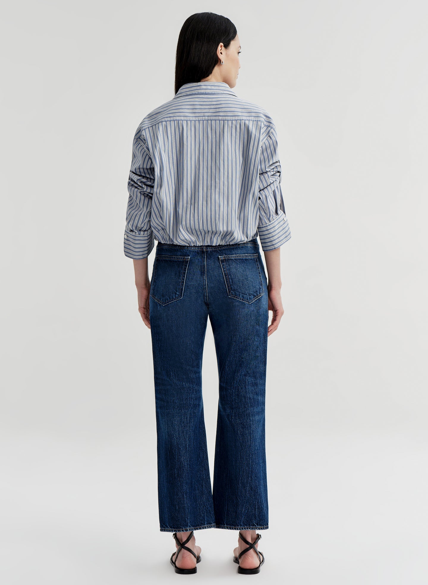 Person wearing a striped shirt and blue jeans on a white background