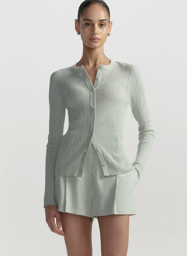 Woman wearing a light green ribbed cardigan over a matching short on a white background
