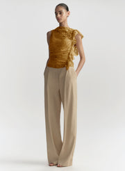 woman in gold lace top and beige pants