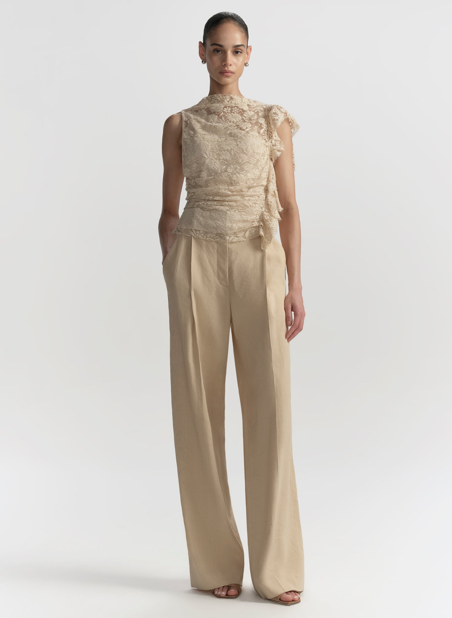 Woman wearing a beige lace top and wide-leg pants on a white background