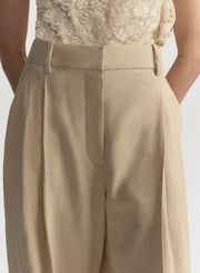 Beige pleated pants worn with a lace top on a plain background