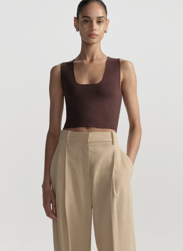 Woman wearing a brown tank top and beige pants against a light gray background