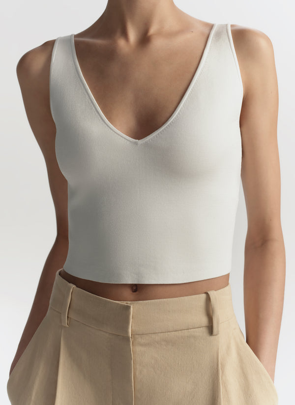 woman wearing a white tank top and beige pants on a plain background