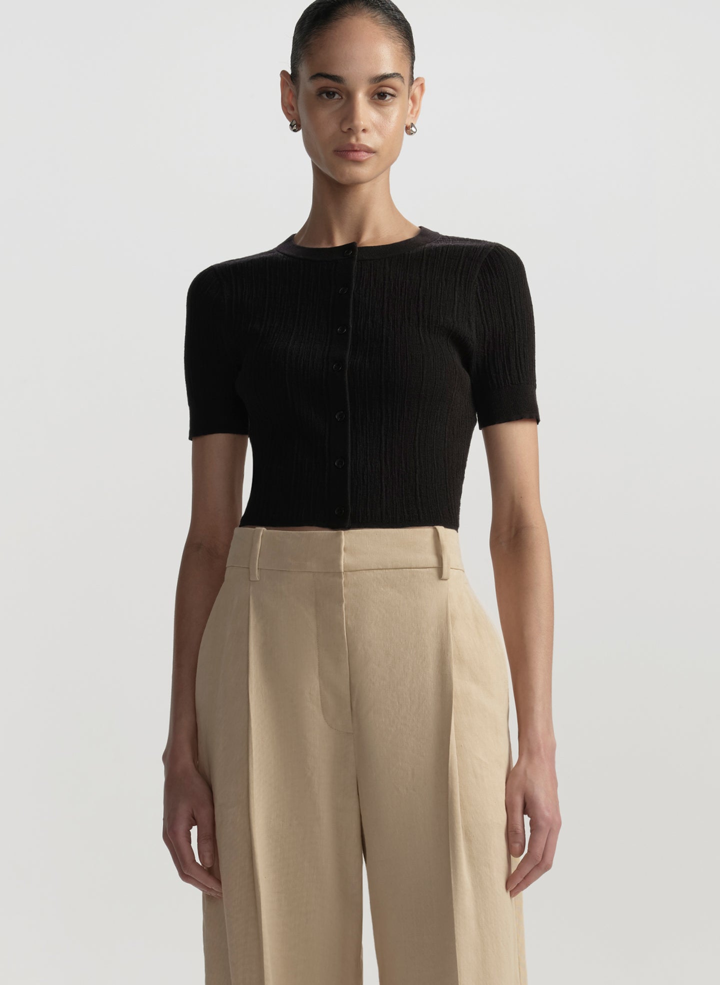 Person wearing a black short-sleeve top and beige pants on a light gray background