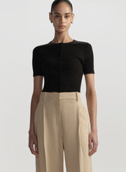 Person wearing a black short-sleeve top and beige pants on a light gray background