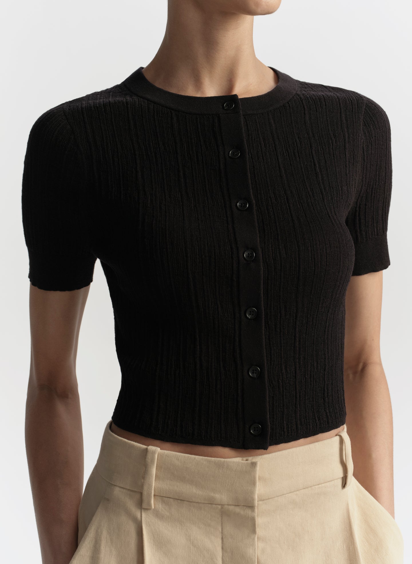 Black ribbed knit cardigan worn by a person on a light gray background