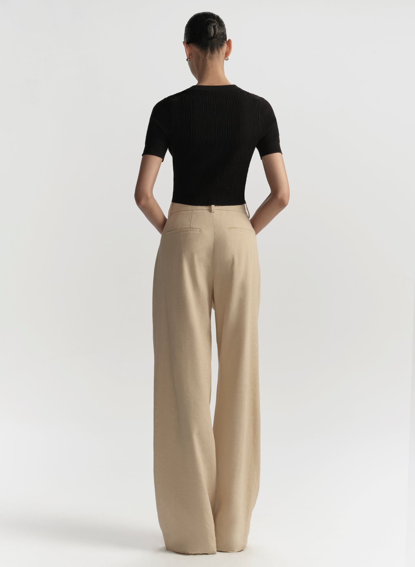 Person wearing a black top and beige pants on a white background